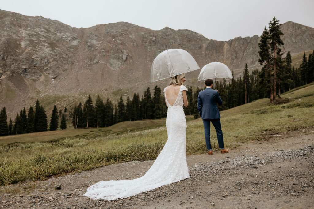 bride and groom stand at base of mountain during first look at ski wedding.