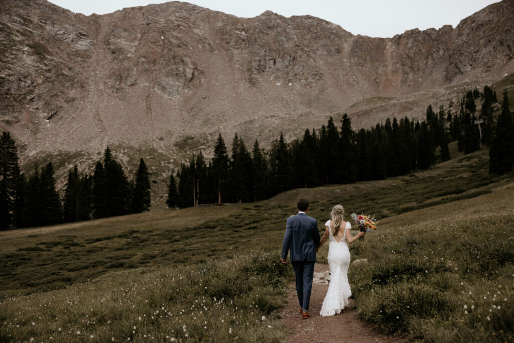 bride and groom walk along trail during their mountaintop colorado micro wedding.