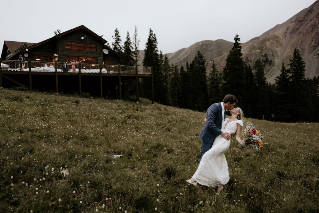 Groom dips bride and kisses her in front of colorado mountain wedding venue