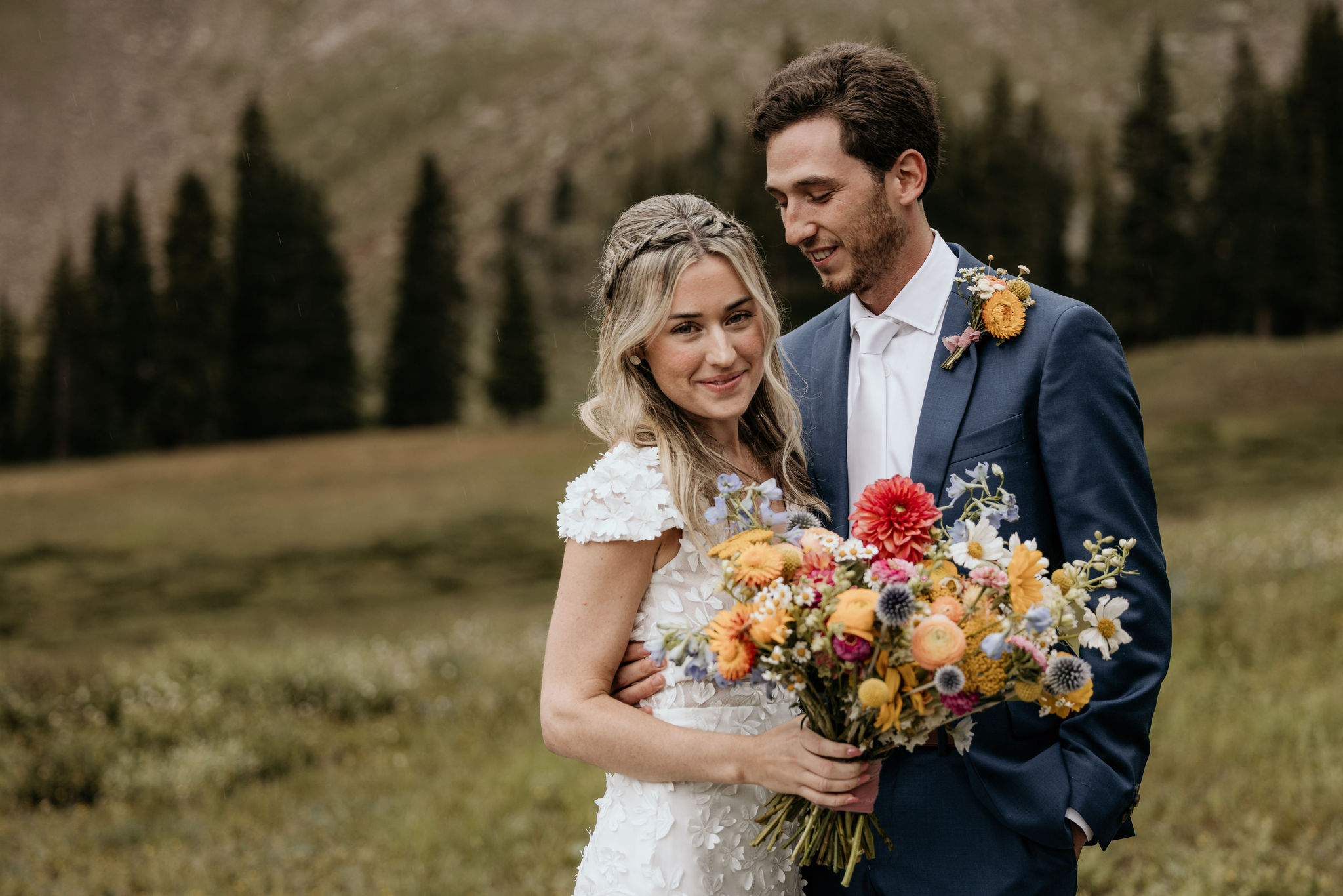 bride smiles at colorado micro wedding photographer as her husband looks at her during their ski mountain wedding at arapahoe basin.