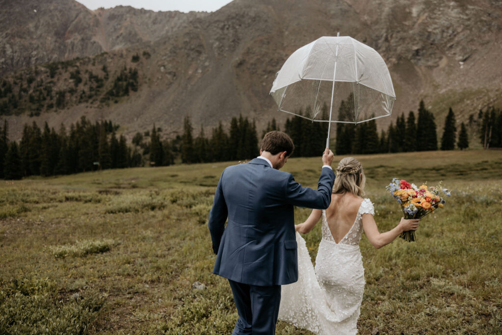 bride and groom walk out into rainy field during their ski wedding in the colorado mountains.
