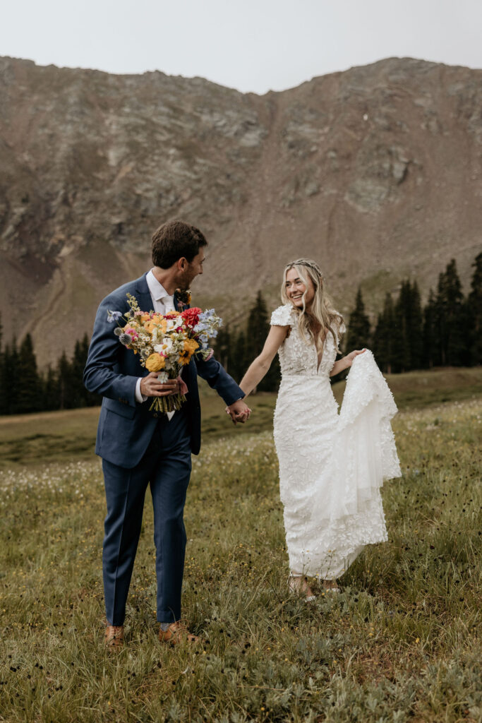 bride and groom hold hands out in the meadow during their ski wedding in the colorado mountains.