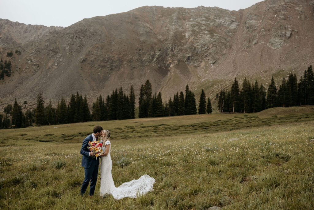 bride and groom kiss in front of mountainside during their ski wedding in colorado.