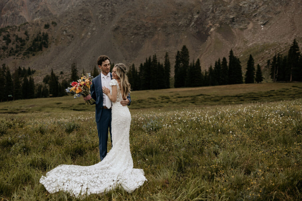 bride and groom embrace in wildflower field during their ski wedding in the colorado mountains.