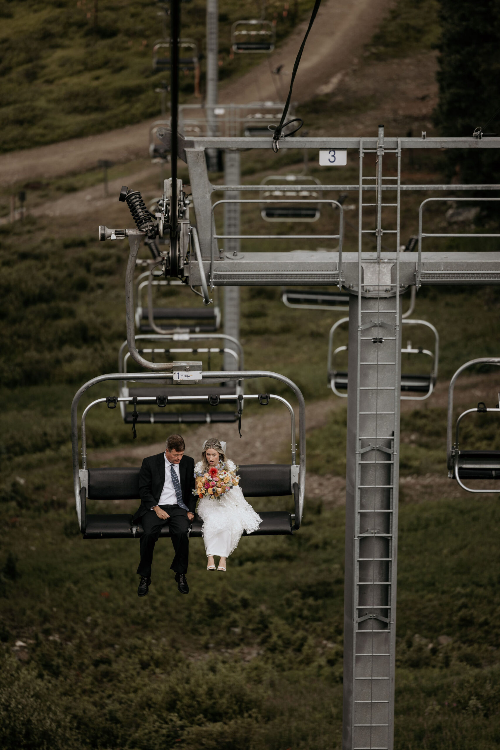 bride rides up ski lift with father on her way to colorado mountain wedding ceremony.