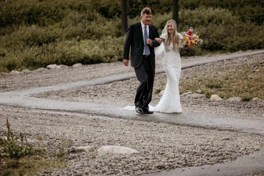 bride and father walk down path to her ski mountain wedding ceremony.
