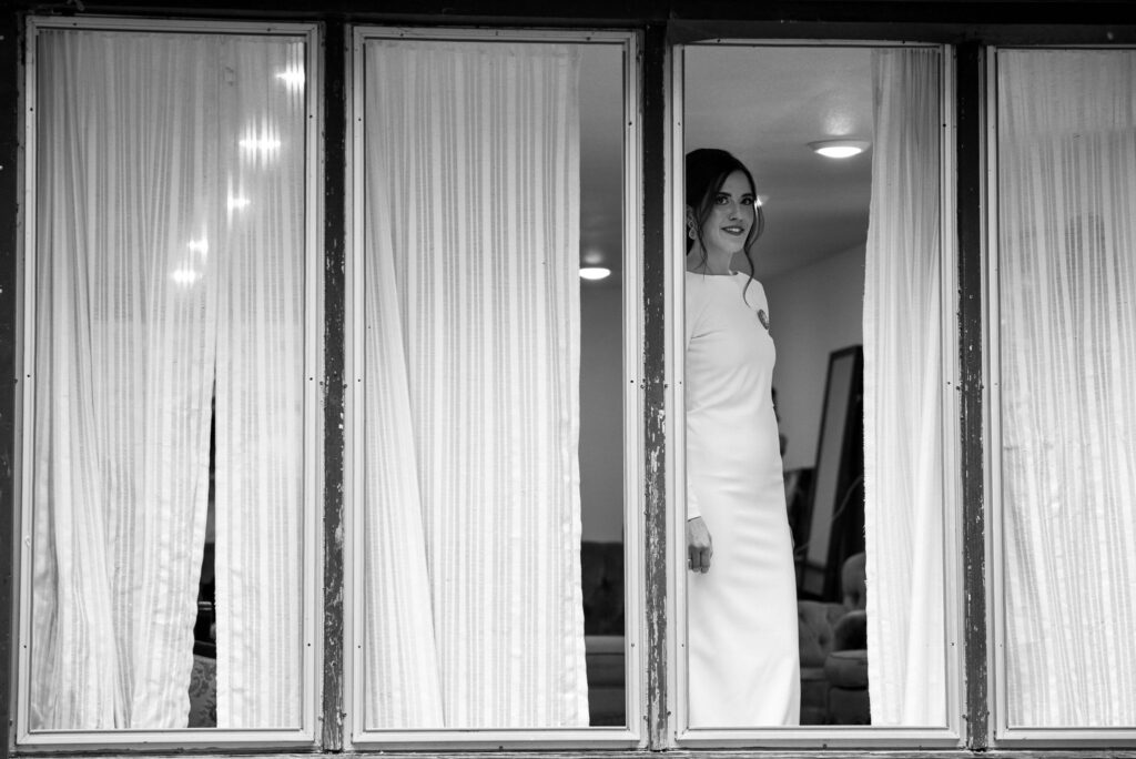 bride stands in the windows of the cottage at river bend for her colorado micro wedding.