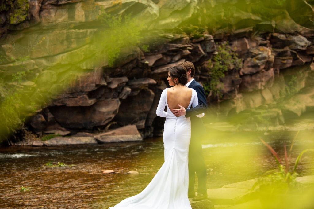 bride and groom stand on rivers edge during micro wedding at river bend venue in lyons colorado.