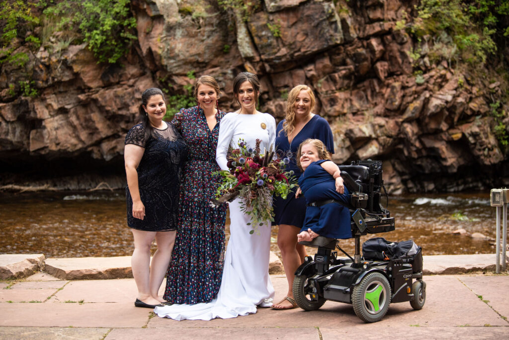 bride and guests stand beside river at River Bend wedding venue in lyons colorado.