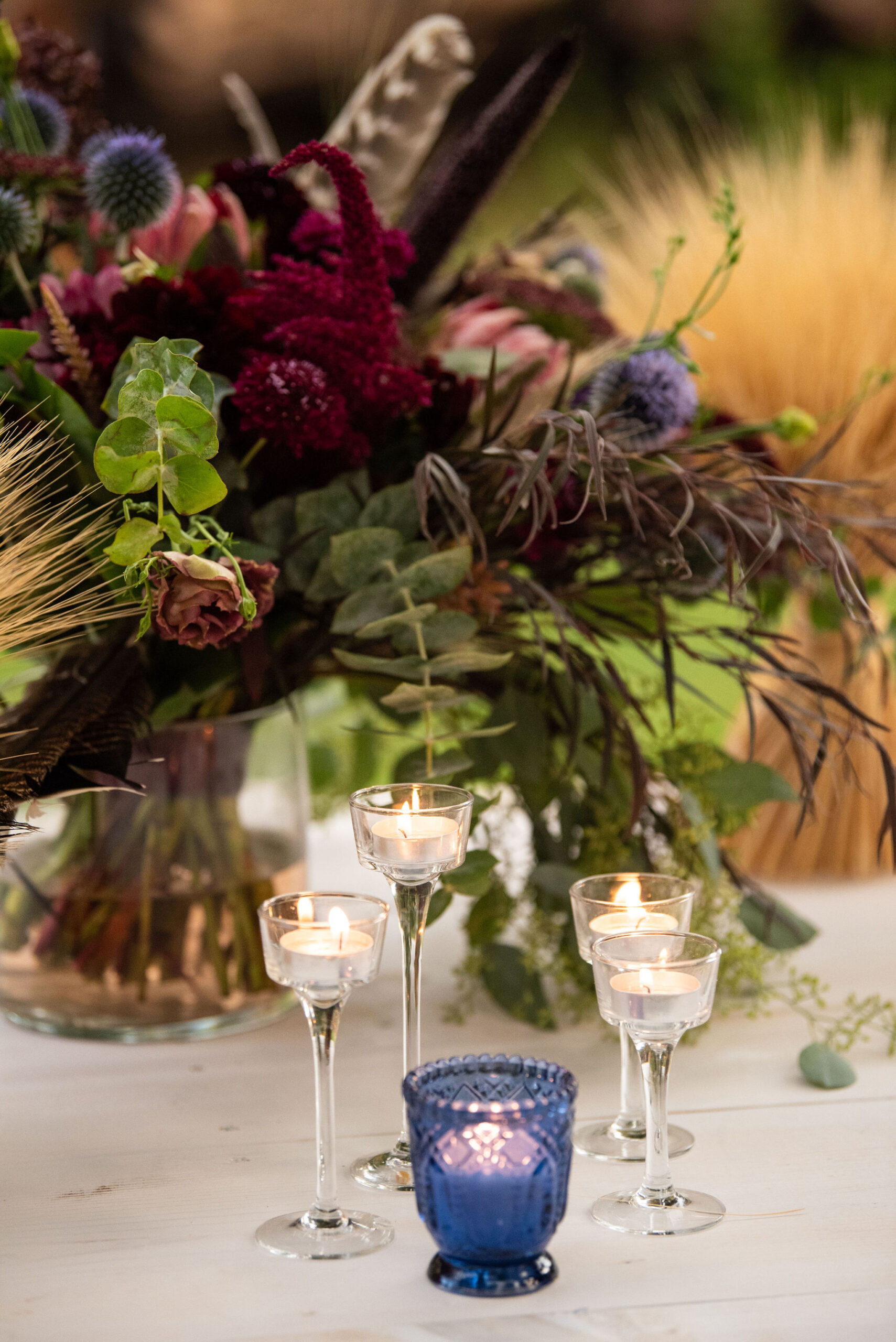 vibrant wedding arrangement by Plume and Furrow sits on the dinner table by candles for a colorado micro wedding at river bend.