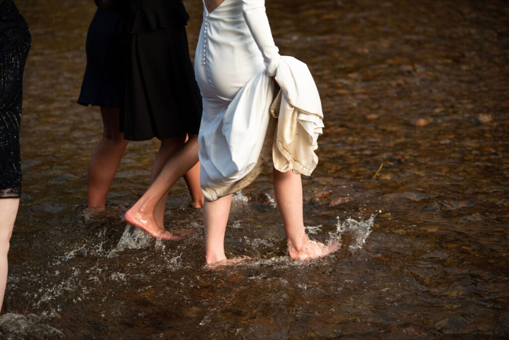 bride and her crew walk in the stream during her micro wedding at river bend wedding venue in colorado.