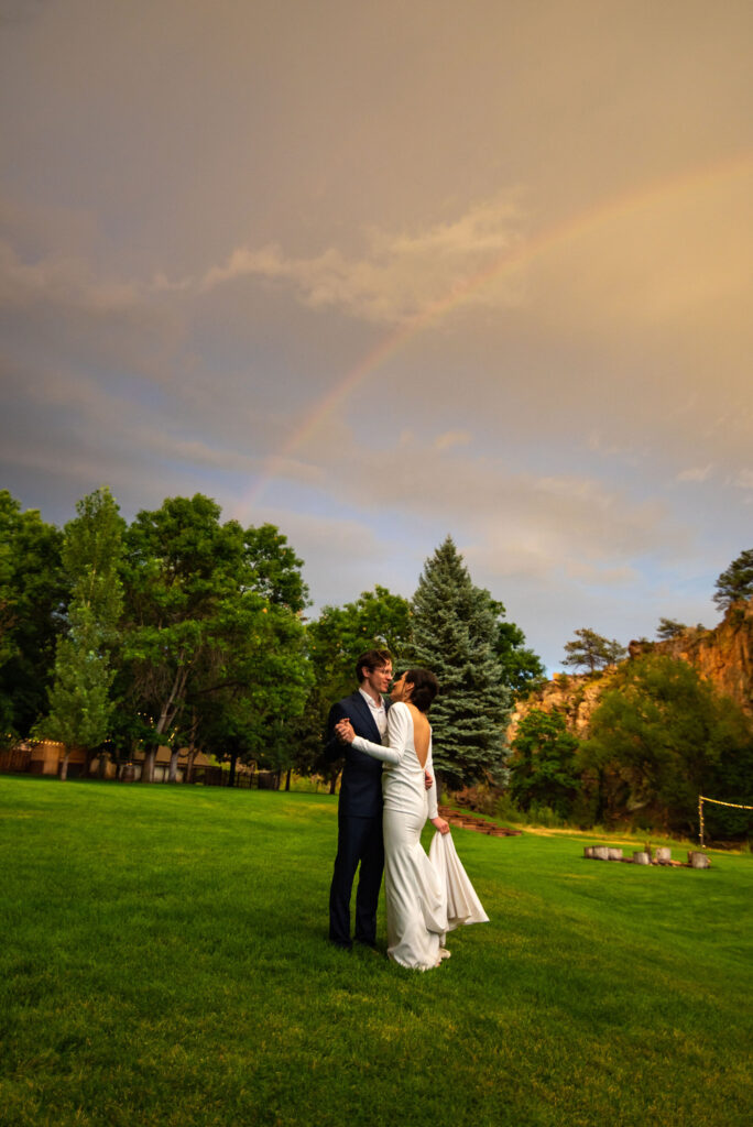 bride and groom dance under double rainbow during colorado micro wedding.