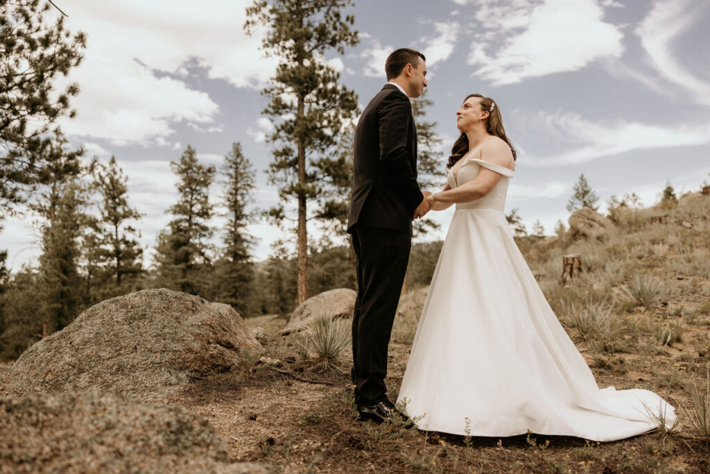 Bride and groom hold hands and smile at each other in the mountains during their fall micro wedding in colorado.