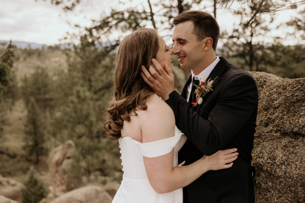 bride and groom lean against rock and embrace during mountain top micro wedding in colorado.