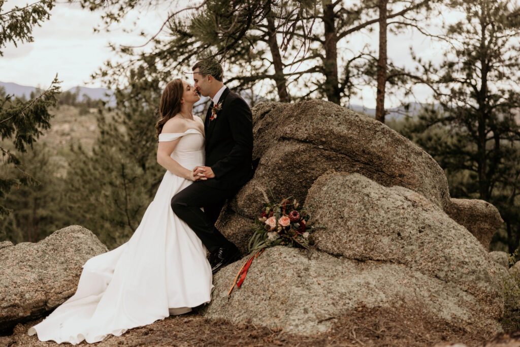 bride and groom lean against rock and kiss during mountain top micro wedding in colorado.