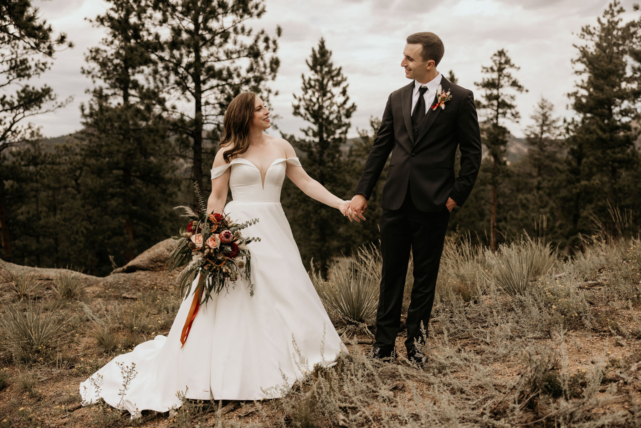 Bride and groom hold hands with the mountains in the background during colorado micro wedding at spires ranch.