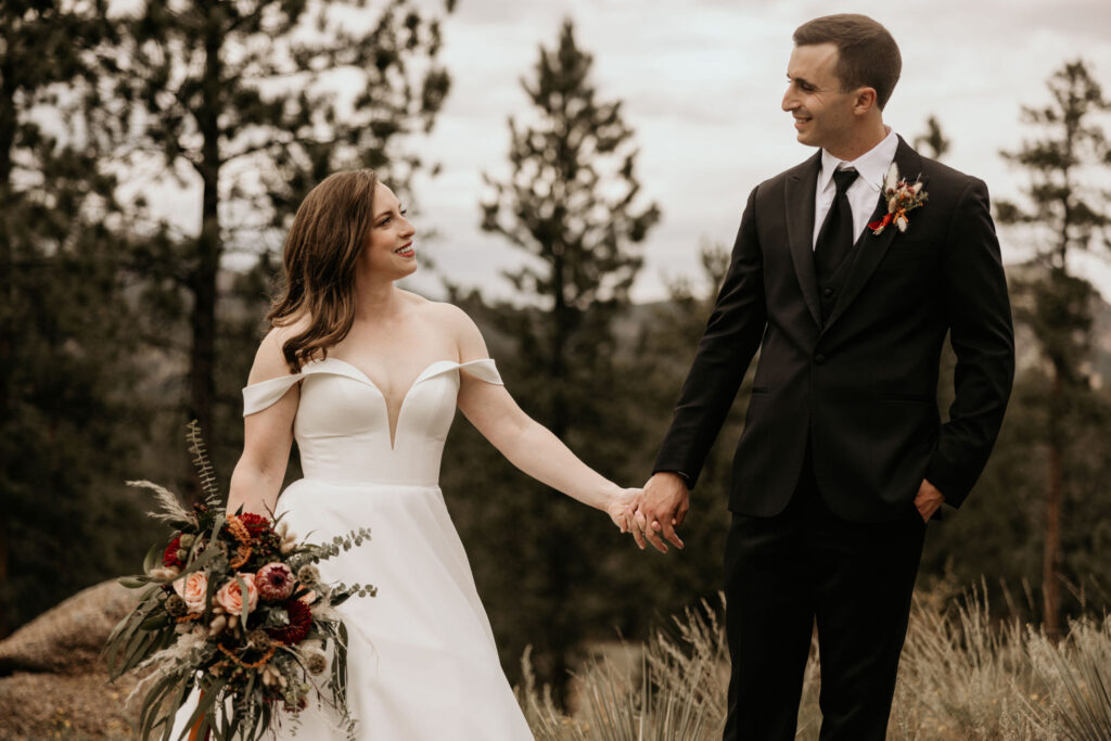 Bride with bouquet and groom hold hands with the mountains in the background during colorado micro wedding.