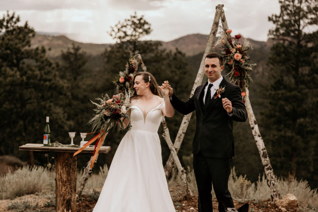 Bride and groom celebrate and hold hands during micro wedding ceremony in the colorado mountains.