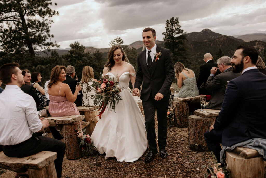 Bride and groom hold hands and walk down aisle during micro wedding ceremony in the colorado mountains.