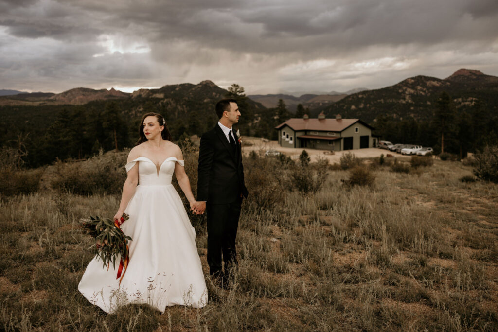 bride and groom hold hands and face away at the mountains, with the wedding venue in the background, during their colorado micro wedding.