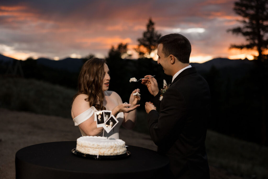 Bride and groom share wedding cake during sunset at their mountaintop micro wedding in colorado.
