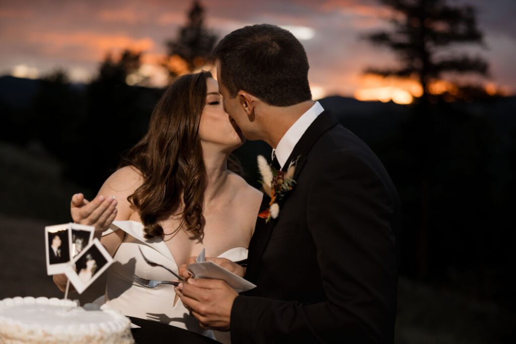 bride and groom kiss and cut cake in front of the sunset during their mountain top micro wedding in colorado.