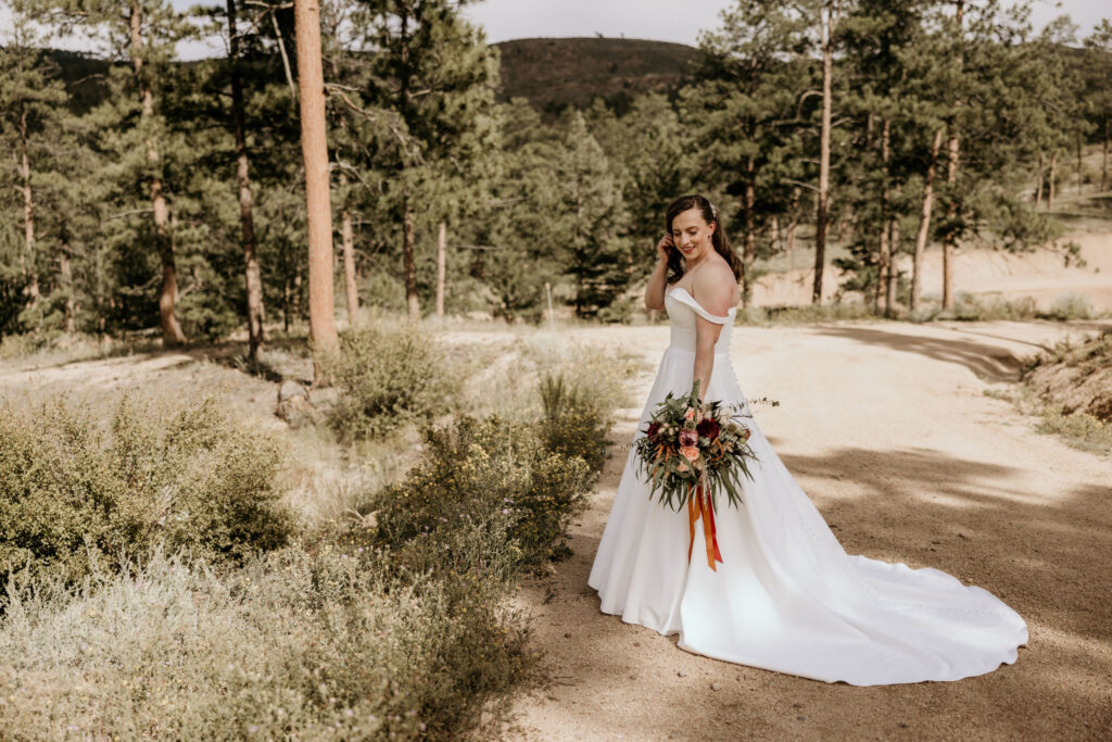 bride stands on trail and holds bouquet outside with the mountains in the background during colorado micro wedding.