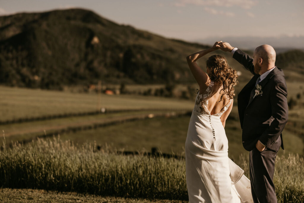groom twirls bride with grassy mountains in the background, during summer wedding in colorado.