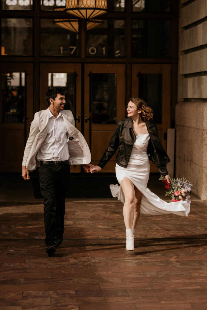 Bride and groom hold hands and walk on sidewalk during their winter micro wedding in Denver, Colorado.