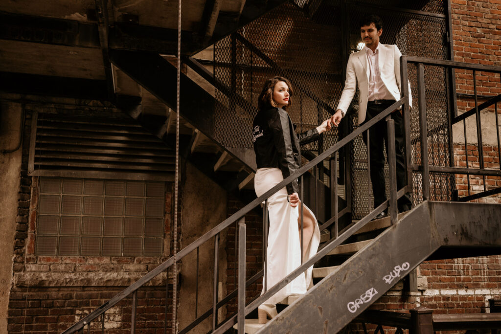 Groom helps bride up stairs of the fire escape during winter urban elopement in downtown denver.