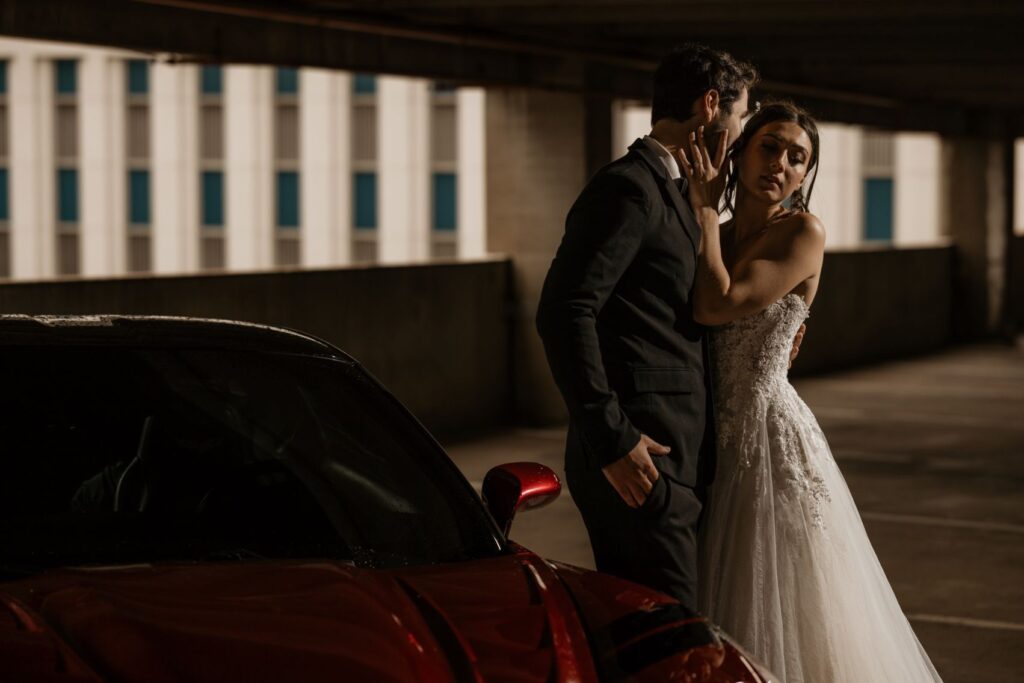 newlywed couple poses for denver wedding photographer beside red car during bridal portrait photos.