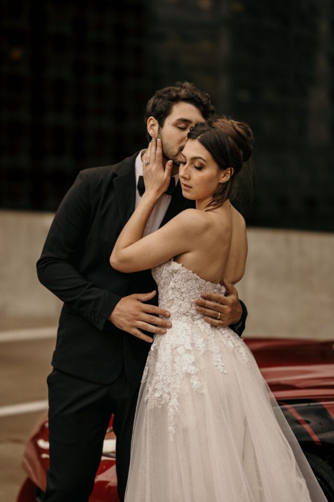 groom kisses brides cheek as they pose on parking garage for urban bridal portraits.