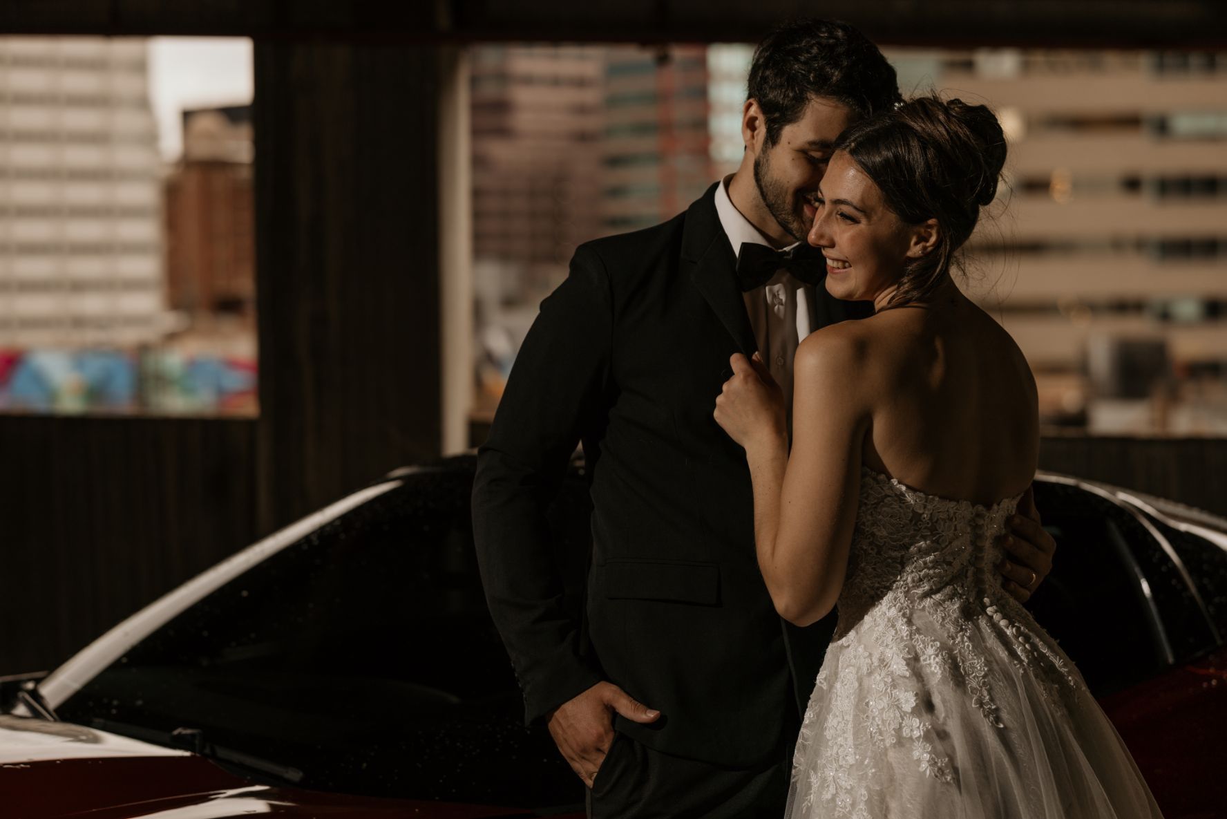bride and groom pose beside red car during bridal portrait session in downtown denver.