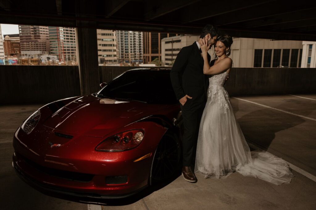 groom and bride stand beside red sportscar during urban bridal portrait session.