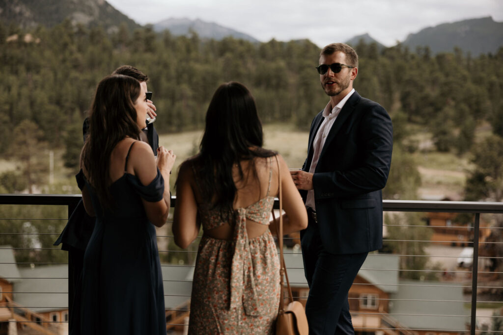 wedding guests mingle on the deck during colorado mountain wedding in estes park.