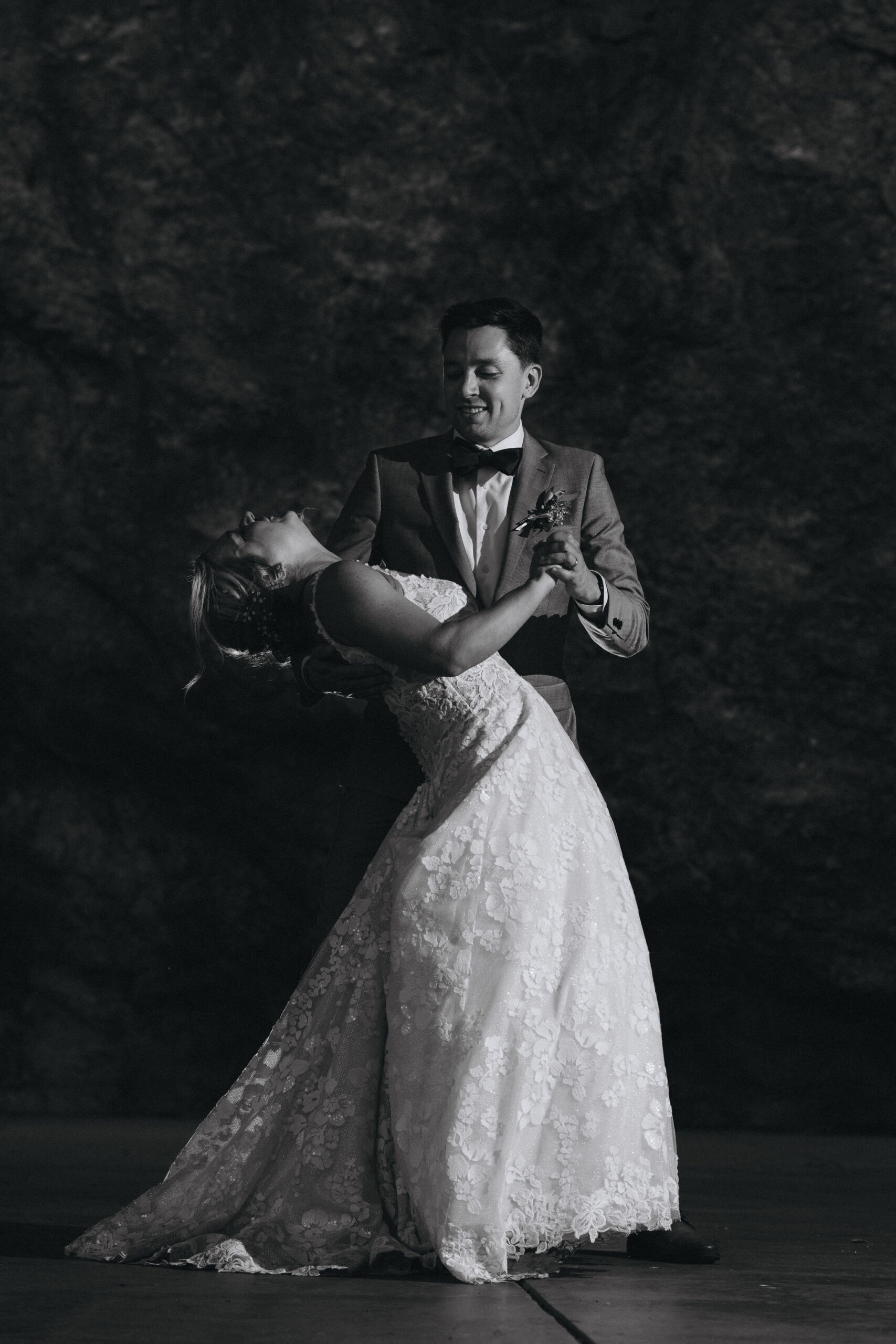 black and white image of bride and groom dancing by rock wall during wedding at skyview venue in estes park colorado.