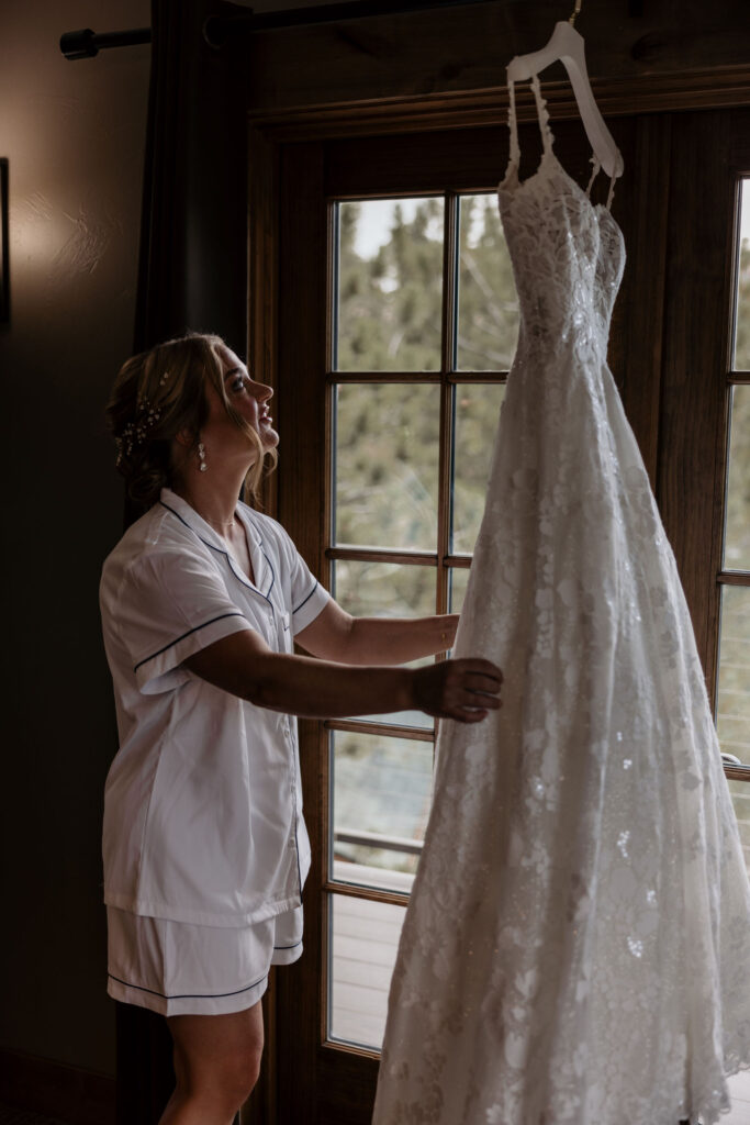 bride looks at hanging dress while getting ready for her colorado wedding in estes park.