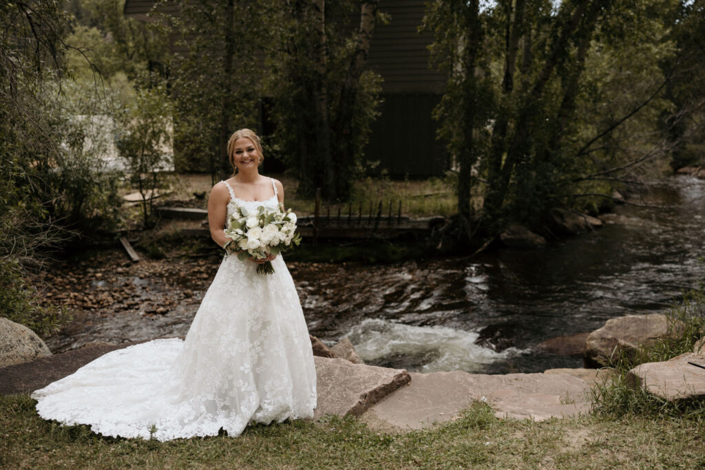 bride stands by river at skyview wedding venue during her mountain wedding in colorado.