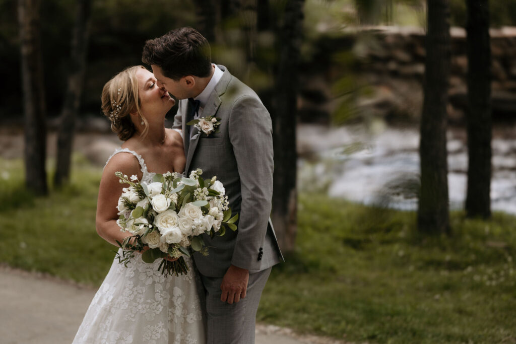 bride and groom kiss by river at skyview wedding venue for their colorado wedding.