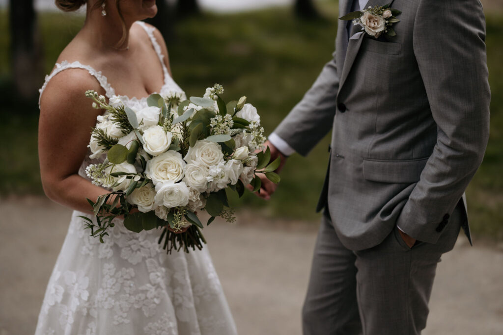 bride and groom hold hands, also holding a floral bouquet, during first look at their colorado wedding at skyview venue.