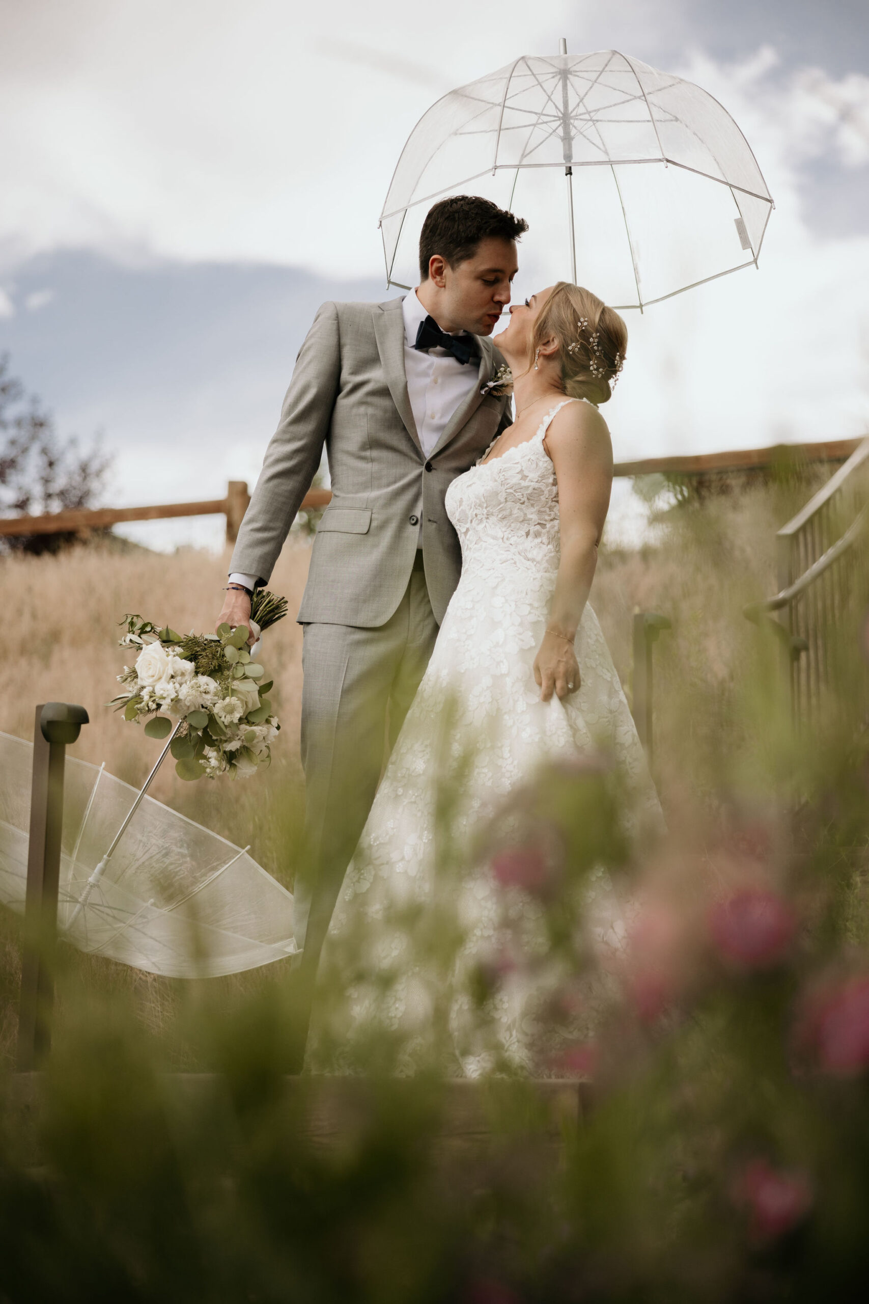 bride and groom kiss under clear umbrellas during mountain wedding in estes park colorado.