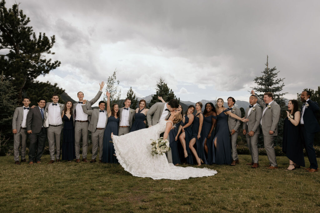 groom dips bride and kisses her with wedding party in the background during colorado mountain wedding in estes park.
