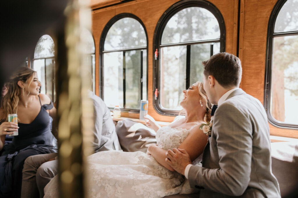 bride, groom, ad guests smile and laugh inside of vintage trolley during eco friendly wedding in colorado.