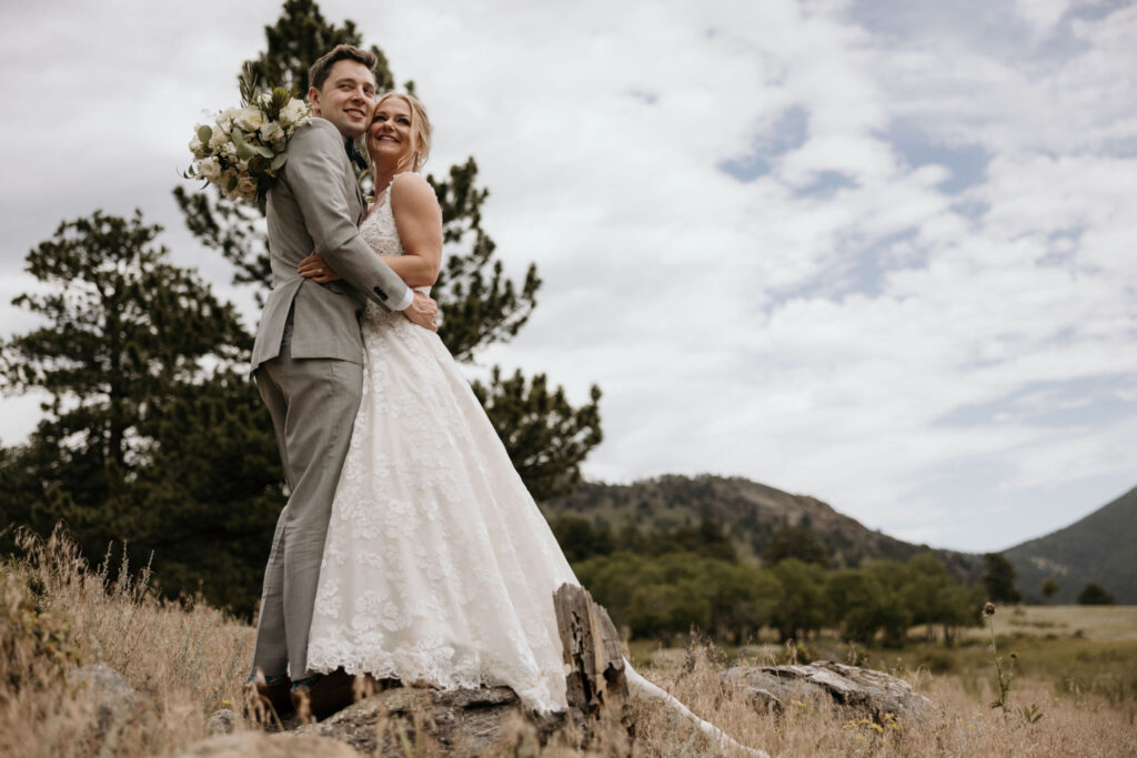bride and groom stand on rock and smile during wedding portraits at rocky mountain national park.