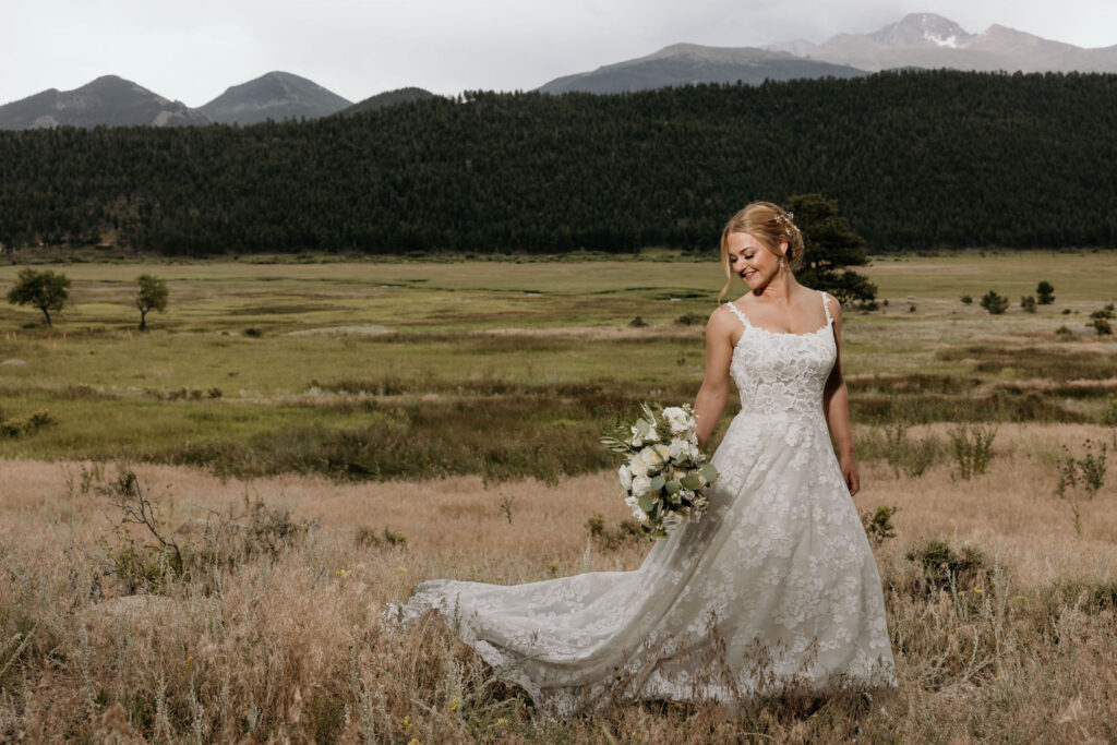 bride stands in front of rocky mountains and smiles with her bouquet during colorado wedding in estes park.