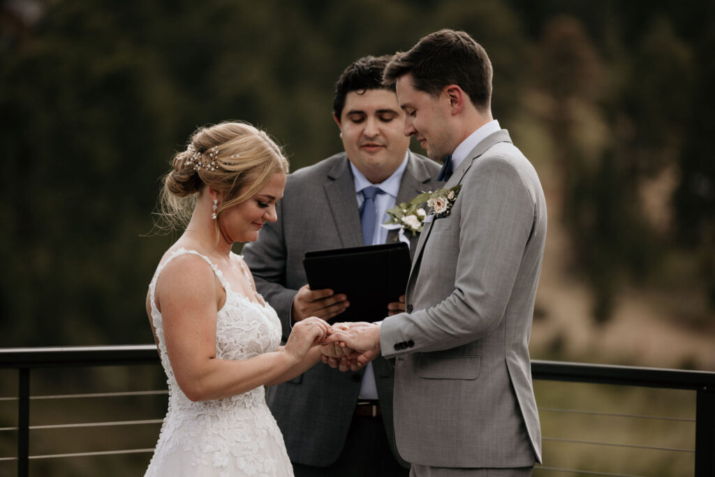 bride puts ring on grooms finger during wedding ceremony at skyview venue in colorado.