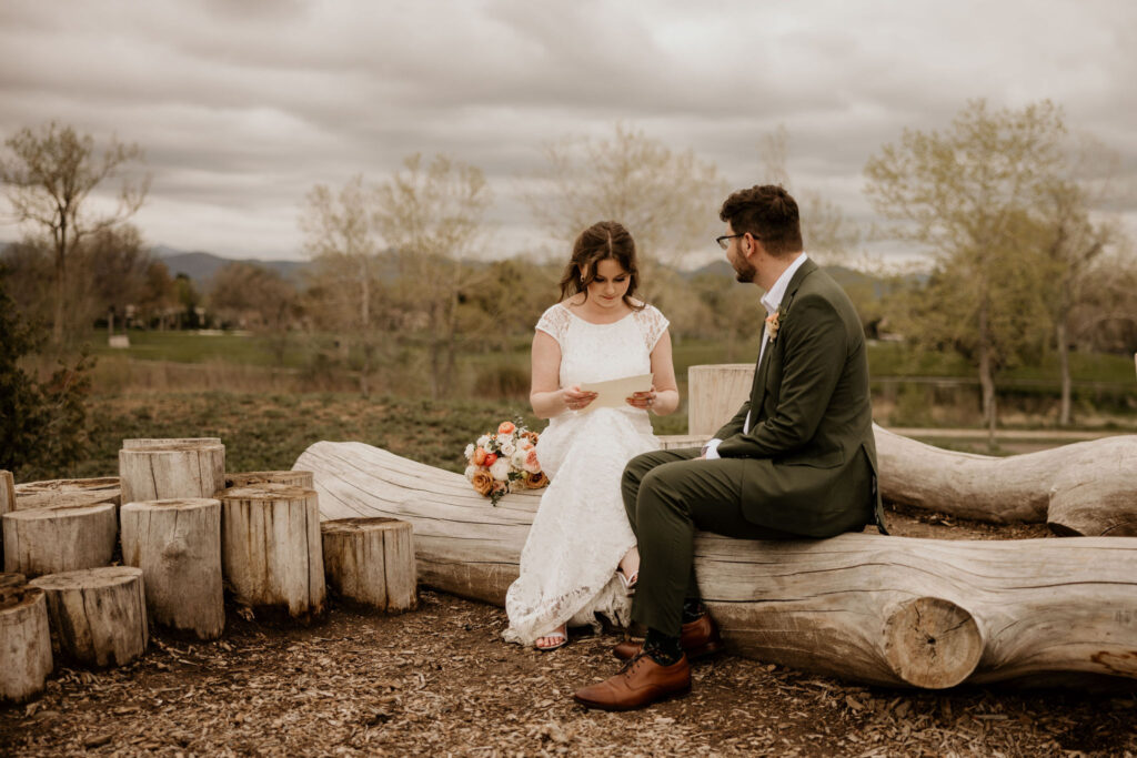 bride reads personal letter from groom, sitting on logs during colorado garden micro wedding in the spring.