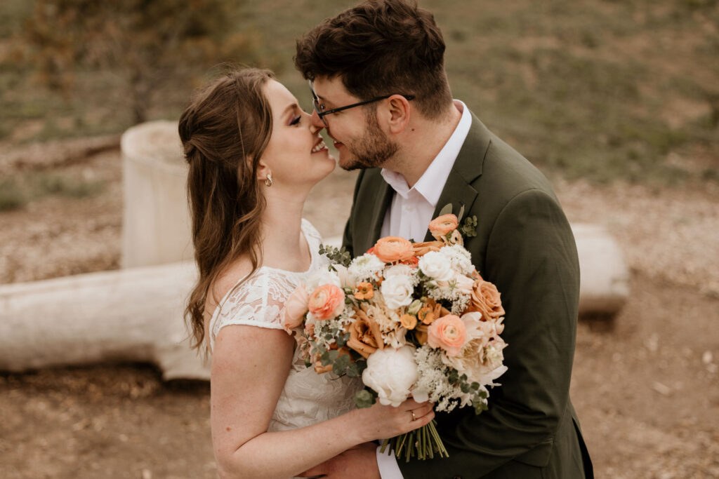 bride and groom kiss with floral bouquet in hand, during eco friendly wedding in colorado.