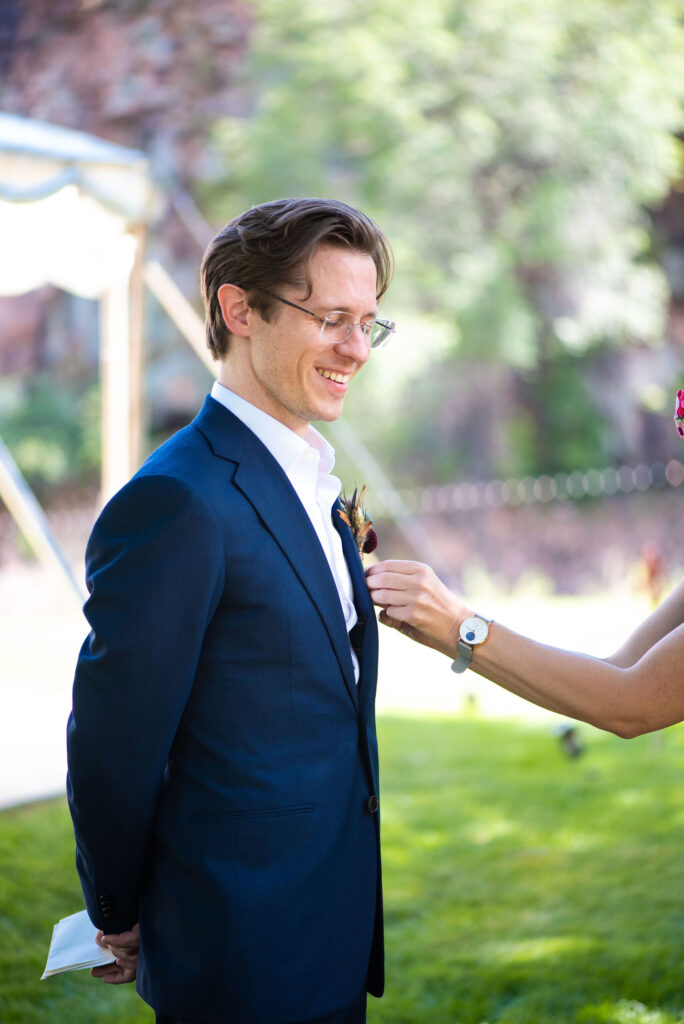 groom gets his boutonniere help during colorado micro wedding in lyons.
