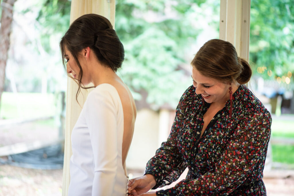 brides friend helps her button her dress for her colorado micro wedding.